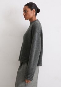 Grauer gestrickter Pullover mit hohem Kragen, senkten Schultern und geripptem Saum. Weiche Textur, mit langen Ärmeln und lässiger Passform.