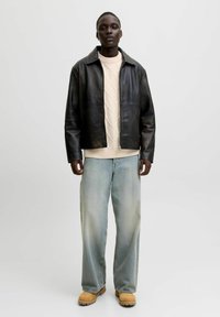 Schwarze Lederjacke mit Kragen, cremefarbener Strickpullover, hellblaue weite Jeans und braune Stiefel. Minimalistisches Design, glatte Textur.