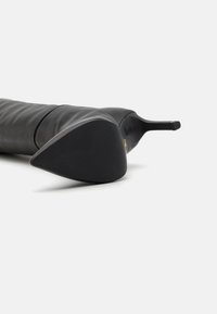 Juodas odinis iki kelių stiletto botas su smailiu pirštu, pasižymintis lygiu paviršiumi ir matinėmis juodomis padais. Minimalistinis dizainas be matomų akcentų.
