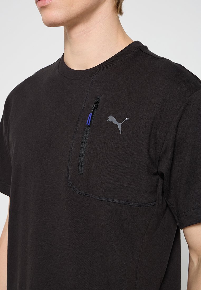 Camiseta de algodón negra con mangas cortas, que cuenta con un bolsillo con cremallera en el pecho y un logo de Puma gris en el lado izquierdo.