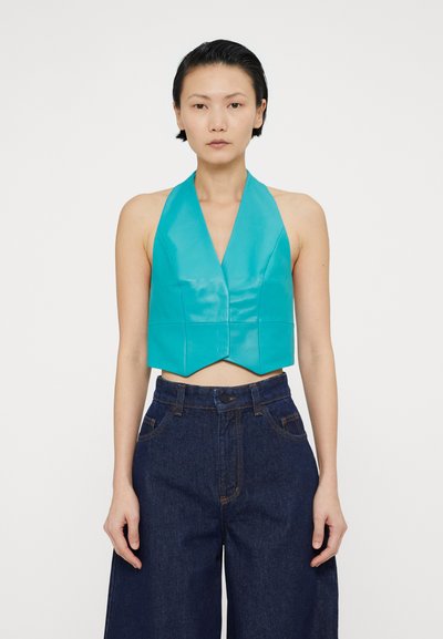 Türkiisi kropped halter-top, mis on valmistatud sujuvast, läikivast materjalist, V-kaelusega ja terava äärisega. Kombineeritud kõrge vöökohaga denim-pükstega.