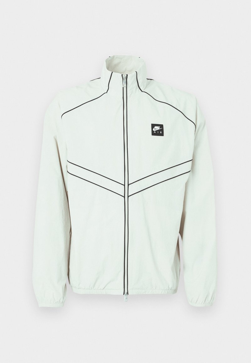 Chaqueta blanca ligera con cuello alto, cierre negro y logo bordado. Cuenta con ribetes negros y puños elásticos para un ajuste ceñido.