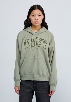 Olive green zip-up hoodie with "OBEY" printed in dark green, featuring a drawstring hood and front pockets, made of soft cotton material.