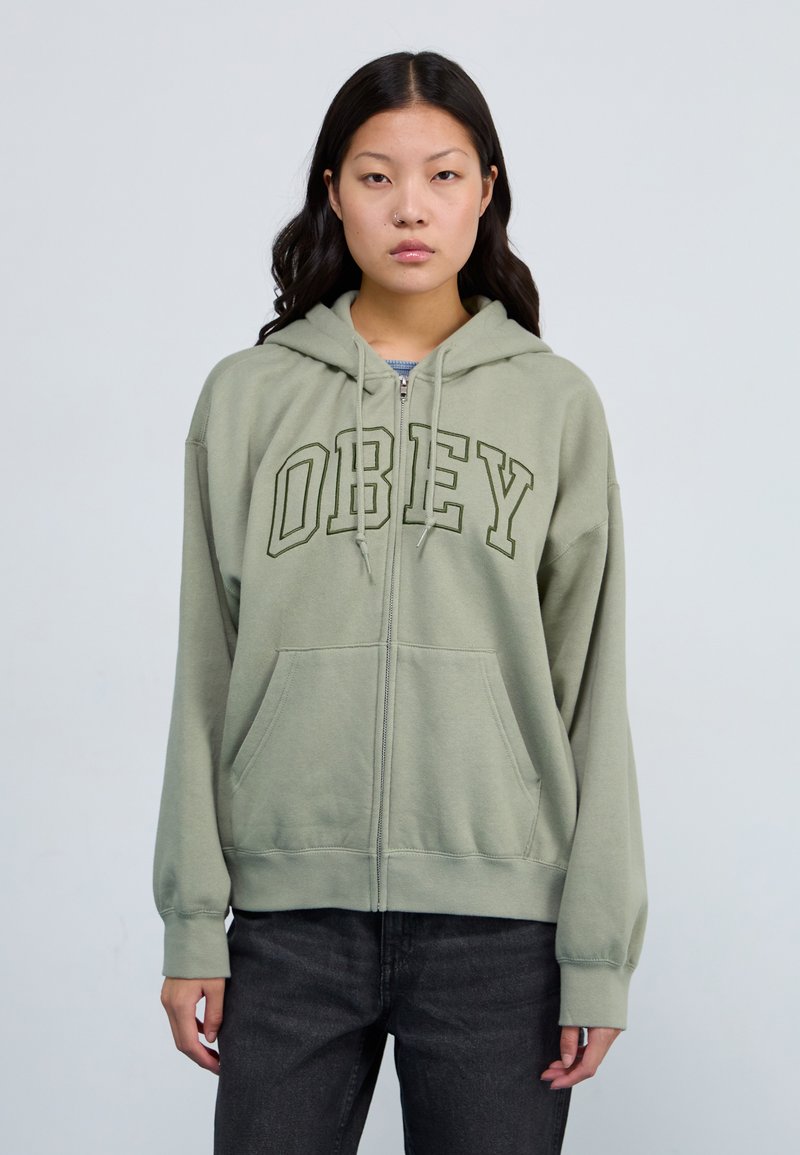 Olive green zip-up hoodie with "OBEY" printed in dark green, featuring a drawstring hood and front pockets, made of soft cotton material.