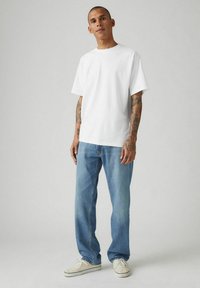Camiseta de algodón blanca de manga corta y cuello redondo, combinada con jeans de pierna recta de color azul claro y zapatillas blancas. Diseño minimalista.