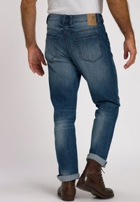 Pantalones vaqueros de mezclilla azul oscuro con un ajuste tapered, con puños enrollados, dos bolsillos traseros y una etiqueta de cuero de la marca en la cinturilla.
