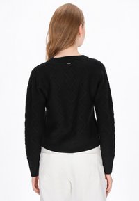 Zwarte trui met textuurpatronen en een cropped ontwerp, met ribbelboorden aan de mouwen en onderkant. Op de achterkant is een subtiele logo-detail zichtbaar.