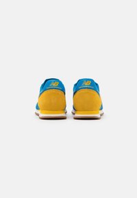 Baskets en suédine bleue et jaune avec une semelle intermédiaire blanche, présentant le logo New Balance en jaune sur le talon et une semelle en caoutchouc texturée.