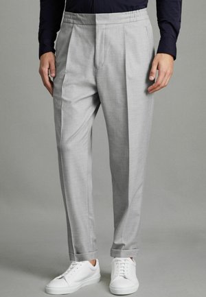 Pantalones plisados de color gris claro con cinturilla elástica y bolsillos laterales, combinados con zapatillas blancas, hechos de una tela suave.