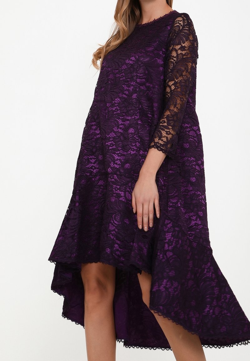 Robe en dentelle violette avec un ourlet asymétrique. Manches longues en dentelle transparente et motifs floraux délicats. Doublure lisse.