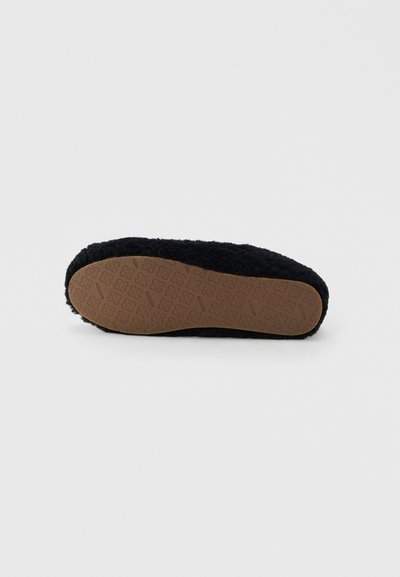 Chausson noir duveteux montré du dessous, avec une semelle en caoutchouc marron ornée d'un motif floral pour adhérence.