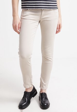 Beżowe spodnie o dopasowanym kroju noszone z czarnymi sznurowanymi butami i czarno-białą paskowaną bluzką, pokazane od talii do stóp.