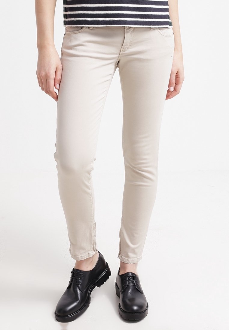 Pantalon beige slim-fit porté avec des chaussures noires à lacets et un haut rayé noir et blanc, montré de la taille aux pieds.