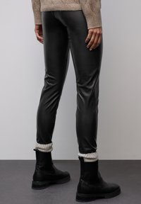 Černé legíny z umělé kůže se slim fit, s hladkým povrchem a manžetami u kotníků, spárované s černými botami a svetrem světle hnědé barvy.