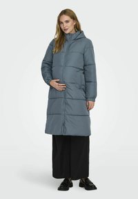 Manteau matelassé longueur cheville en gris doux avec fermeture éclair à l'avant, poches latérales et capuche. Présente des coutures horizontales pour une texture ajoutée.