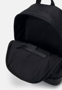 Černý batoh s hladkým matným povrchem. Interiér obsahuje měkkou látkovou podšívku a klopu se zipovým uzávěrem. Minimalistický design.