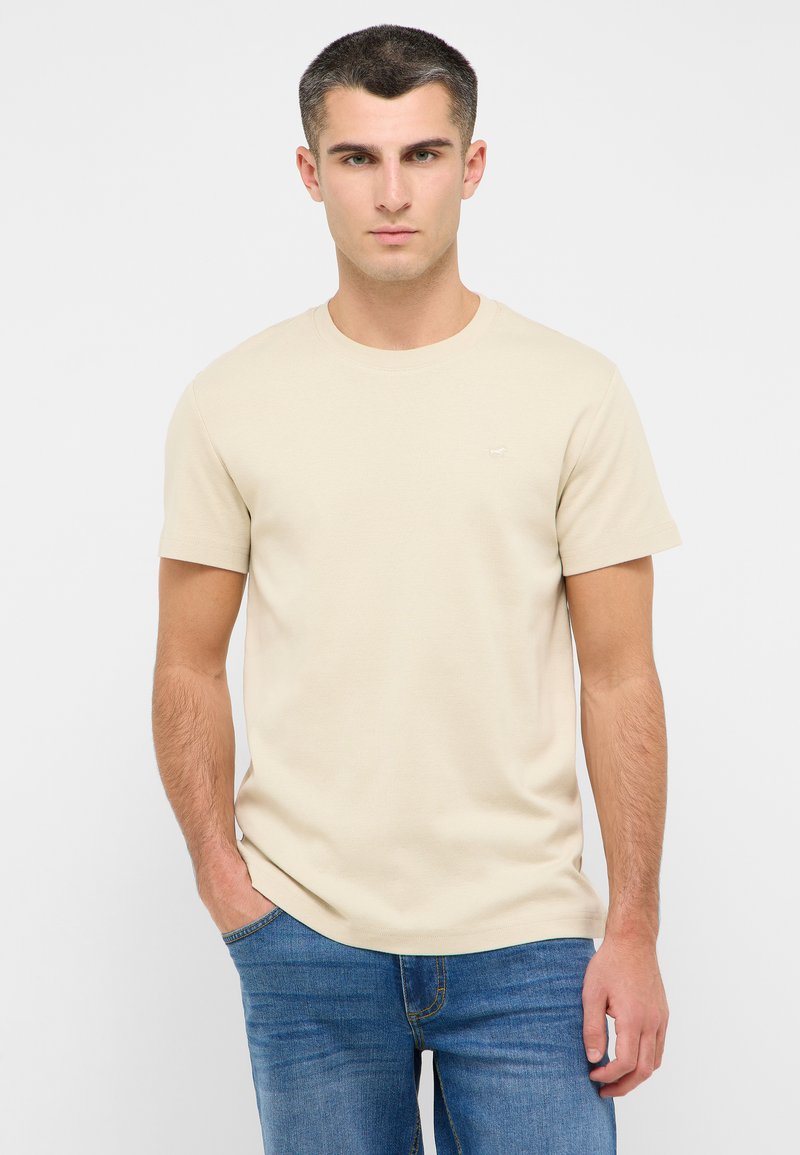 Beige T-Shirt mit Rundhalsausschnitt aus Baumwolle, mit kurzen Ärmeln und strukturiertem Finish. Ein kleines Logo ist auf der Brust sichtbar.