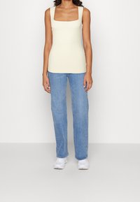 Ärmelloses, geripptes Tanktop in hellgelb, kombiniert mit geraden blauen Jeans und weißen Sportschuhen. Einfaches Design und taillierte Form.