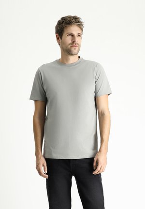 Camiseta de manga corta gris claro hecha de una tela suave, con un cuello redondo y un diseño simple, combinada con jeans oscuros.