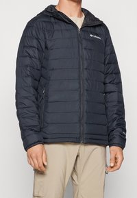 Czarna, wyściełana kurtka z suwakiem z przodu i kapturem. Posiada poziome przeszycia i boczne kieszenie, wykonana z lekkiego, wodoodpornego materiału.