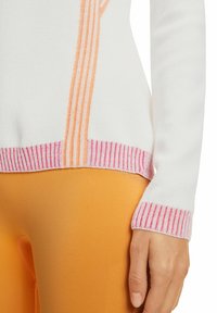 Maglione bianco con accenti a strisce arancioni e rosa, polsini e orlo a costine. Texture morbida, design aderente abbinato a leggings arancioni.