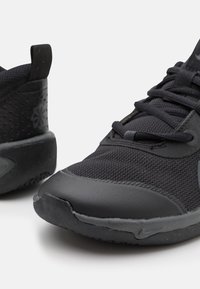 Black athletic sneakers with mesh fabric, rubber soles, lace-up fronts, and a pull tab on the heel against a plain white background.