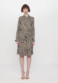 Long-sleeve shirt dress featuring a geometric print in beige and navy, with a fitted waist and ruffled cuffs. Smooth fabric texture.