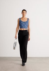 Top corto de mezclilla con patrón geométrico, combinado con pantalones negros de talle alto. El sujeto sostiene un bolso metálico y lleva botas de tacón negras.