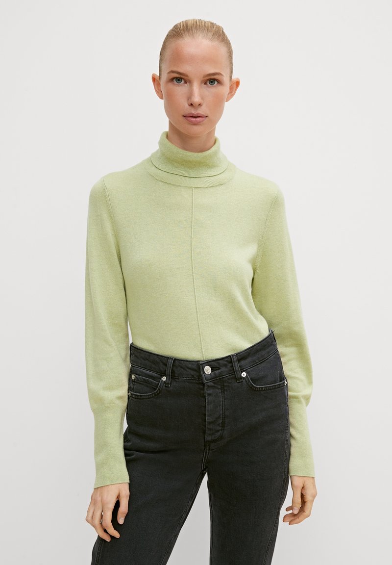 Light green turtleneck sweater in soft fabric, featuring a fitted design, long sleeves, and a ribbed neckline, paired with black jeans.