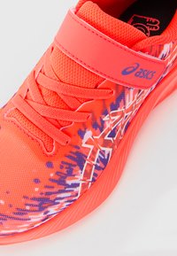 Baskets de sport pour enfants en corail vif avec des motifs graphiques en violet et blanc, une sangle Velcro portant l'inscription "asics" et des lacets assortis.