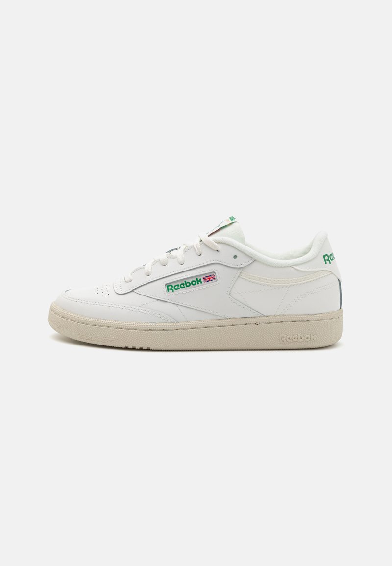 Sneaker bianca in pelle con una suola in gomma naturale testurizzata color tan, dettagli in logo verde e un design low-top con chiusura a lacci e perforazioni.