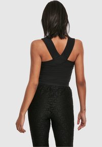 Schwarzes ärmelloses Top mit überkreuzten Trägern, kombiniert mit schwarzen, strukturierten Hosen mit floraler Spitze. Das Design ist enganliegend und glatt.