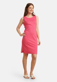Roze mouwloze jurk met een ronde halslijn, aansluitend ontwerp en zijsplitten. Gladde stofstructuur, knielengte, gecombineerd met lichte sandaaltjes.