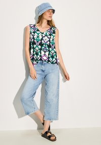 Top senza maniche con un motivo geometrico multicolore in verde, viola e nero; abbinato a jeans cropped azzurri e sandali neri.