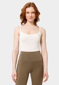 Bílý přiléhavý top na tenk é ramínka s hladkým povrchem, mírně vykrojený výstřih, zkombinovaný s kalhotami v olivově zelené barvě s vysokým páskem.