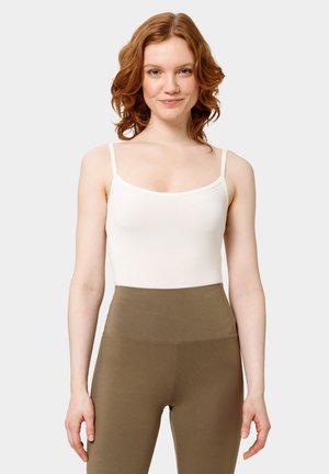 Top sin mangas blanco ajustado con tirantes delgados, textura suave, escote ligeramente redondeado, combinado con leggings verde oliva de cintura alta.