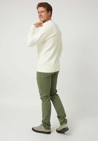 Camisa de manga larga color crema con puños acanalados, combinada con pantalones ajustados verde oliva y zapatillas gris claro, sobre un fondo liso.