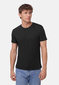 Camiseta de algodón negra con cuello redondo, mangas cortas y un corte casual, combinada con unos vaqueros de denim azul claro.