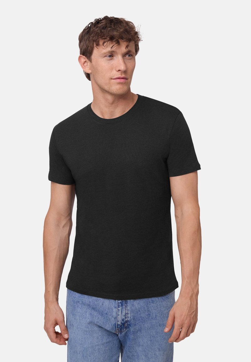 Camiseta de algodón negra con cuello redondo, mangas cortas y un corte casual, combinada con unos vaqueros de denim azul claro.