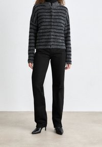 Cardigan de punto a rayas en gris y negro con cuello alto, cierre frontal de botones y mangas largas, combinado con pantalones rectos negros y tacones.