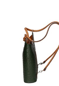 Sac en cuir vert avec une surface texturée et à pois. Il dispose de sangles beige fixées avec du matériel en acier inoxydable, mettant en avant une forme cylindrique unique.