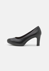 Chaussure à talon noir en matériau synthétique lisse, avec un bout rond, un talon bloc de hauteur intermédiaire et un design minimaliste.