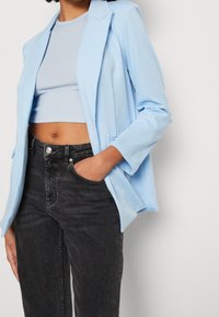 Blazer bleu clair en tissu doux avec un col à revers cranté, associé à un haut clair ajusté et un jean noir taille haute.