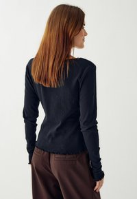 Čierny dlhý rukáv s textúrovaným vzorom, priliehavý strih, kordovaný lem a rebrované manžety, v kombinácii s hnedými nohavicami s vysokým pásom.