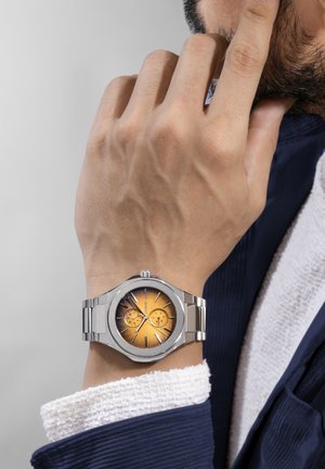 Sølv rustfrit stål ur med et oktagonalt hus, orange solstråledial, to underdials og et børstet metalarmbånd.