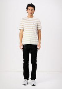Striped short-sleeve t-shirt in beige and cream, featuring a chest pocket, paired with black jeans and white sneakers.