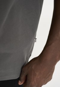 Grå t-shirt lavet af blødt stof, med et enkelt, rundhalset design. Et lille mærke er synligt på siden nær kanten.
