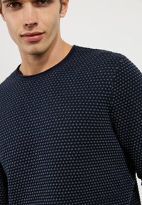 Suéter texturizado en color navy con cuello redondo. Presenta un sutil patrón geométrico en un tono más claro, material suave y un diseño ajustado.
