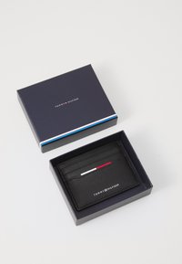 Black leather card holder in a blue box, featuring five card slots and a red and white accent line. "TOMMY HILFIGER" logo displayed.