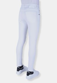 Witte skinny spijkerbroek van denim met een gladde textuur, vijf zakken en zwarte knoopaccenten, gecombineerd met witte sneakers met zwarte details.